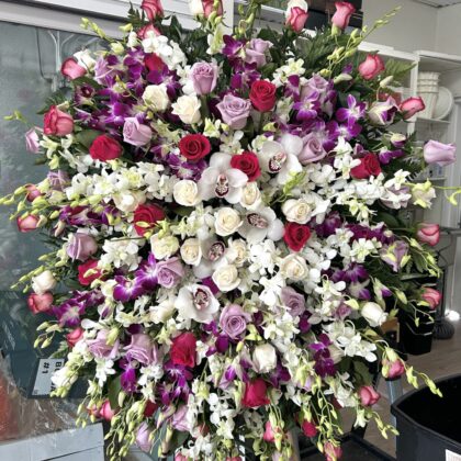 Heavenly Grace Funeral Spray, a luxurious floral display of roses and orchids in shades of deep red, lavender, and white.