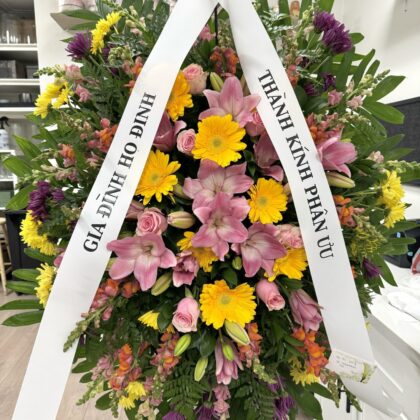 Spark of Memory Funeral Spray - Vibrant Floral Tribute featuring yellow daisies, pink lilies, and roses on a stand.