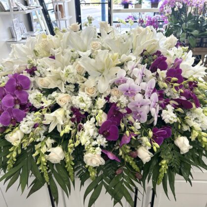 Blanca Blooms Casket Spray - Elegant White Floral Design featuring white lilies, roses, and vibrant purple orchids.
