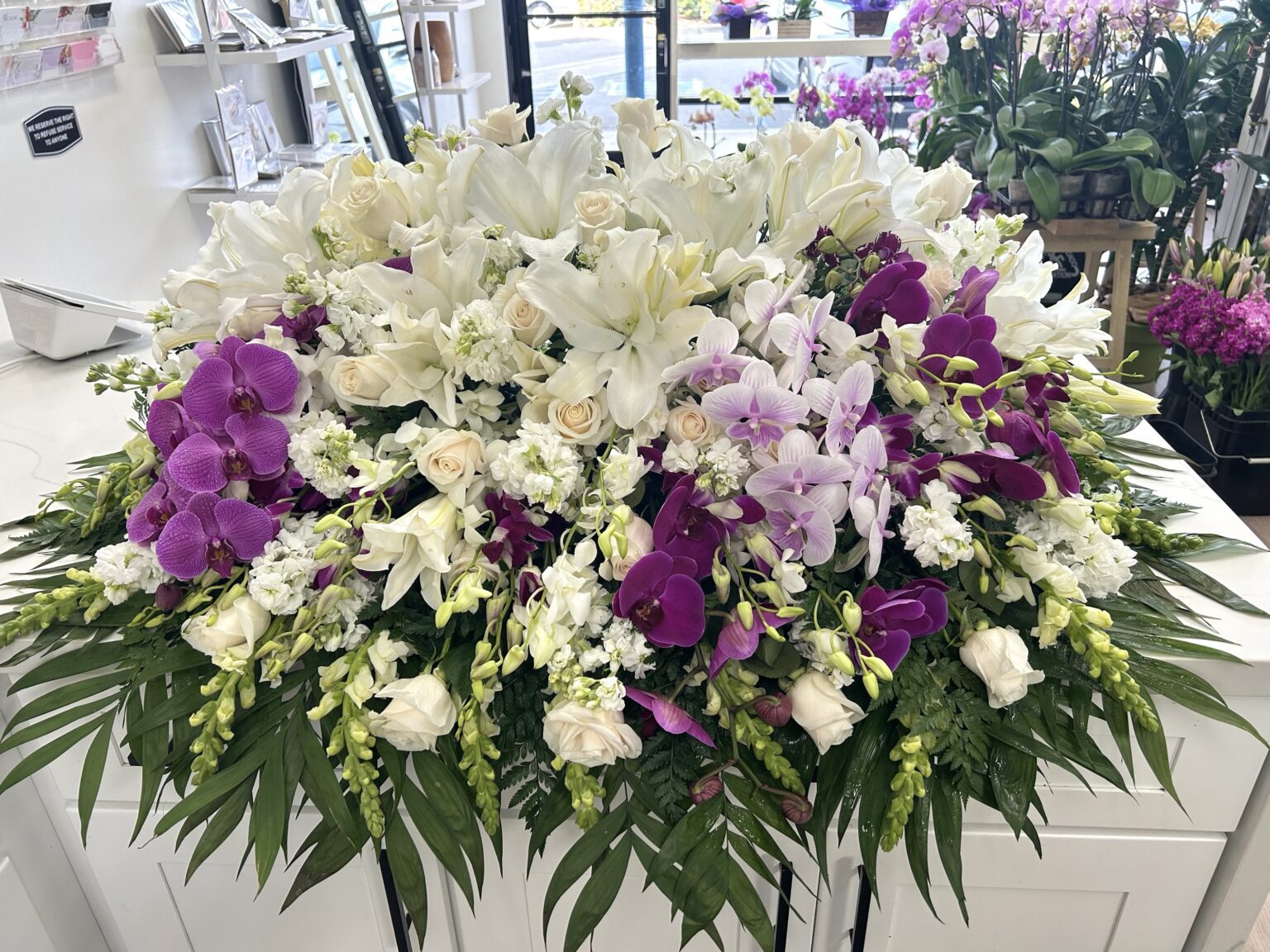 Blanca Blooms Casket Spray - Elegant White Floral Design featuring white lilies, roses, and vibrant purple orchids.
