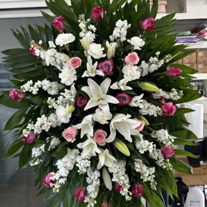 Celestial Comfort &ndash; Stunning Funeral Spray featuring white lilies, pink roses, and white stock flowers on palm leaves.