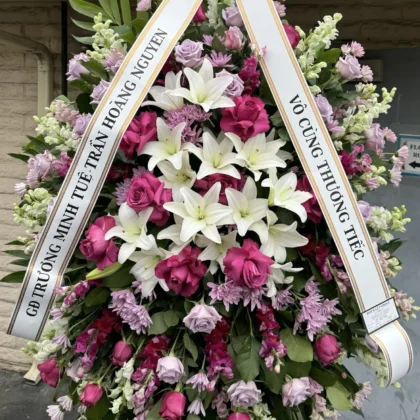 Guardian Angel – Respectful Funeral Spray featuring white lilies, magenta and lavender roses, and snapdragons on a stand.