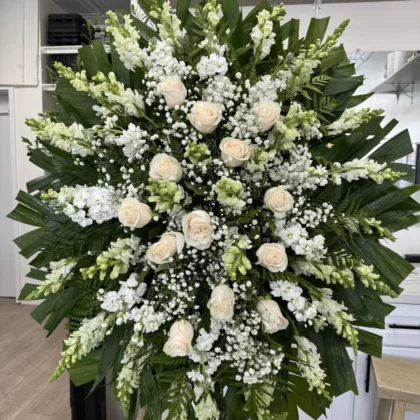Twilight Tribute – Timeless Funeral Spray featuring cream roses, white snapdragons, and baby's breath on palm leaves.