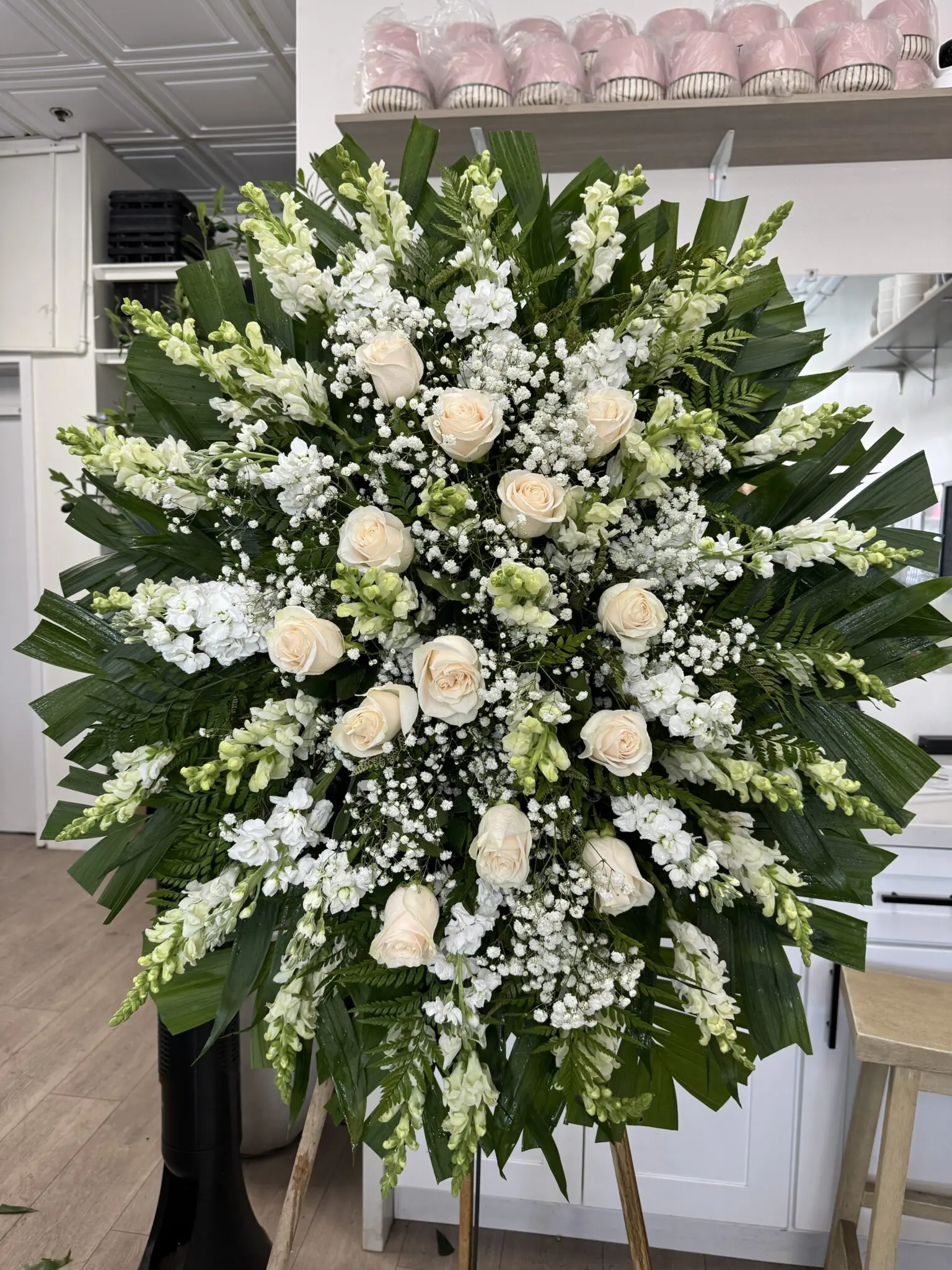 Twilight Tribute – Timeless Funeral Spray featuring cream roses, white snapdragons, and baby's breath on palm leaves.