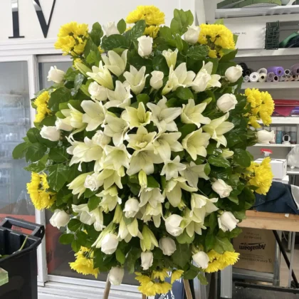 Golden Memories Funeral Spray - Vibrant Wreath featuring white lilies, roses, and yellow chrysanthemums on a stand.