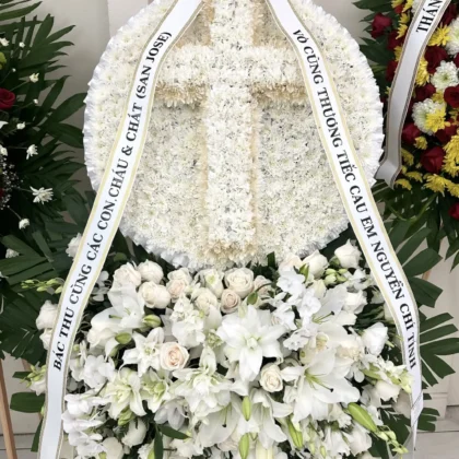 Halo Blooms Cross Funeral Spray - Elegant Design featuring white carnations and lilies in a double-layered arrangement.