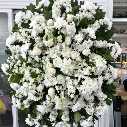 Budding Memories Funeral Spray featuring a circular elegance of white roses, chrysanthemums, and orchids on a stand.