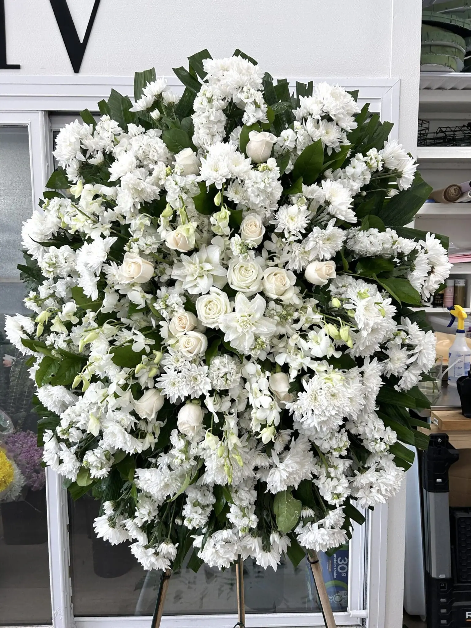 Budding Memories Funeral Spray featuring a circular elegance of white roses, chrysanthemums, and orchids on a stand.