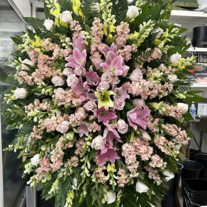 Sweet Memories Funeral Spray, a stunning arrangement of pink lilies, soft roses, and yellow snapdragons on a stand.