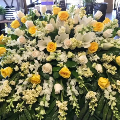 Yellow Dreams Casket Spray – Elegant Floral Tribute featuring yellow roses, white lilies, and stock flowers.