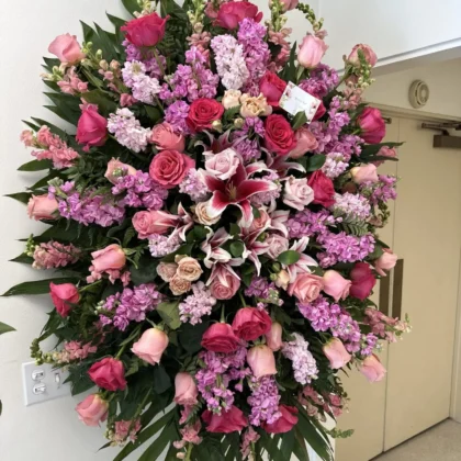 Sweet Serenity Funeral Spray – Lush Floral Arrangement featuring pink roses, lilies, and stock on a standing easel.