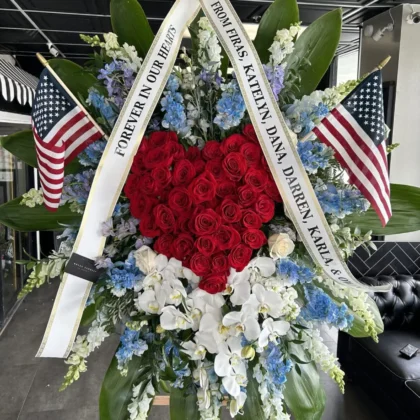 Patriotic Remembrance Funeral Spray – Honor with Pride featuring a red rose heart, blue delphinium, and white orchids.