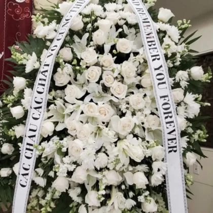 Calm Waters Funeral Spray – Pristine White Elegance featuring lush white roses, lilies, and snapdragons in a grand display.