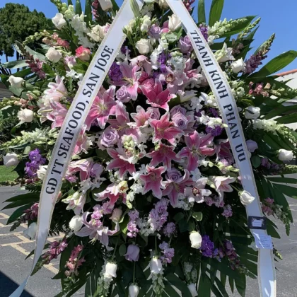 Softly Spoken Funeral Spray for Cherished Memories featuring pink lilies, lavender roses, and white accents on a stand.