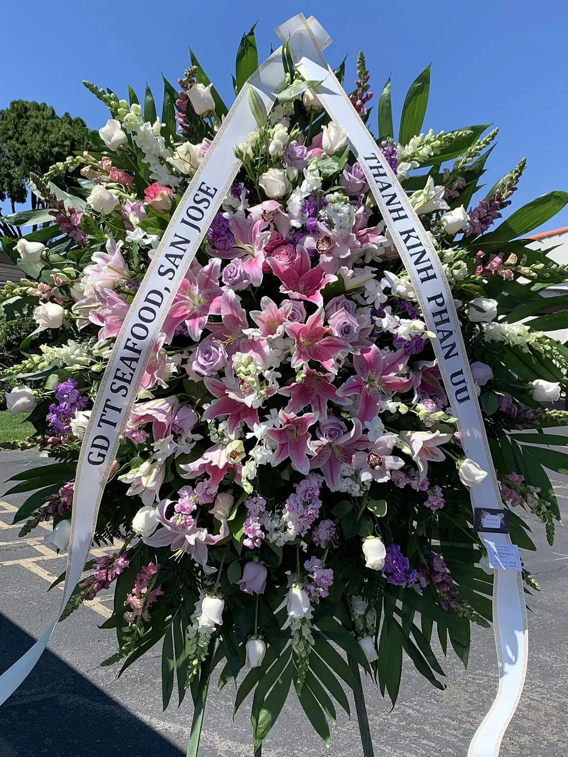 Softly Spoken Funeral Spray for Cherished Memories featuring pink lilies, lavender roses, and white accents on a stand.
