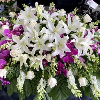 Peaceful Blooms Casket Spray - Traditional Elegance featuring white lilies, roses, and vibrant purple orchids.