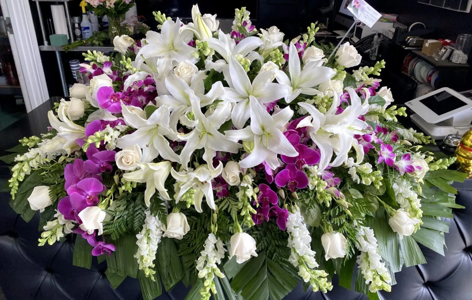 Peaceful Blooms Casket Spray - Traditional Elegance featuring white lilies, roses, and vibrant purple orchids.