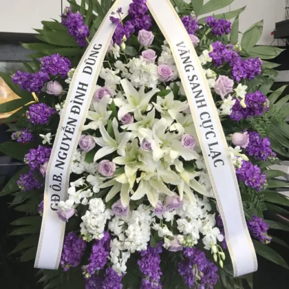 Tender Care Funeral Spray featuring white lilies, purple stock, and lavender roses for a Dignified Presence.