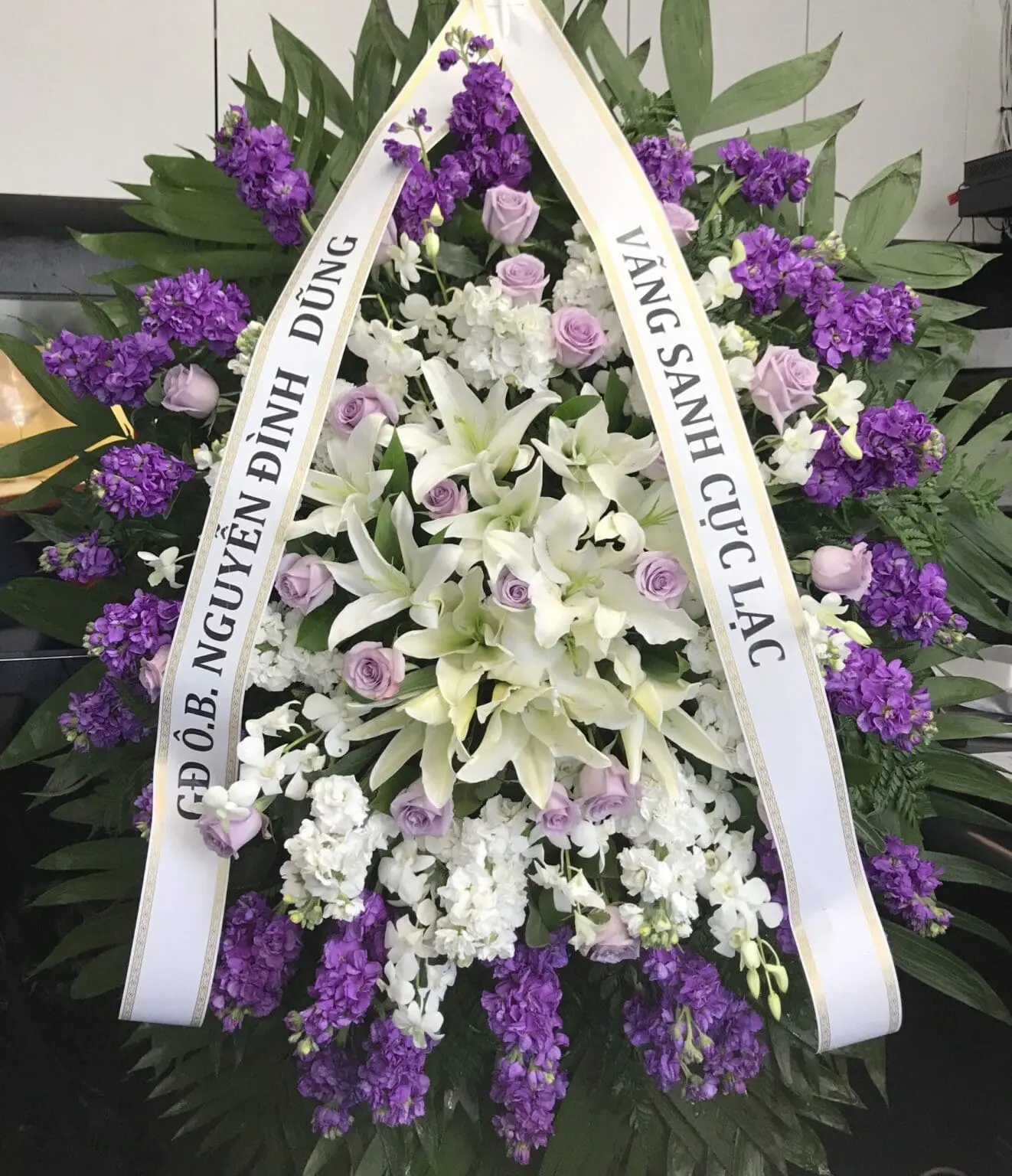 Tender Care Funeral Spray featuring white lilies, purple stock, and lavender roses for a Dignified Presence.