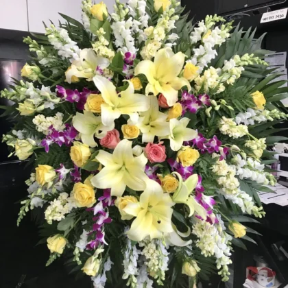 Sweet Peace Funeral Spray - Vibrant Floral Tribute featuring yellow lilies, roses, and purple orchids on a stand.