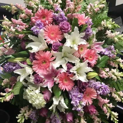 Pillow of Petals Funeral Spray - Vibrant Tribute featuring pink gerberas, white lilies, and lavender roses in a lush arrangement.