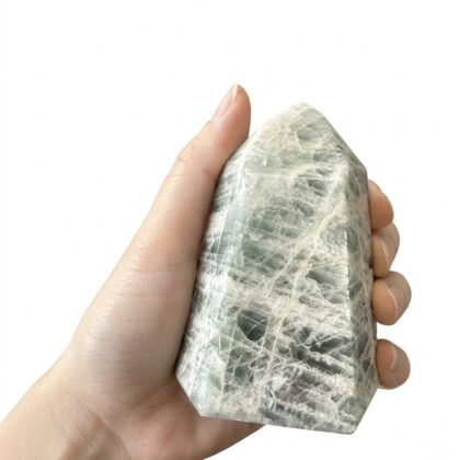 A hand holds a polished, hexagonal crystal tower featuring marbled shades of sage green, grey, and white.