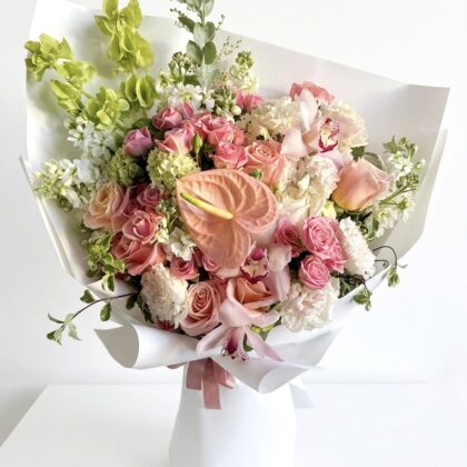 Le Jardin de Versailles – Wrapped Floral Bouquet featuring pink roses, anthuriums, and orchids in white paper.