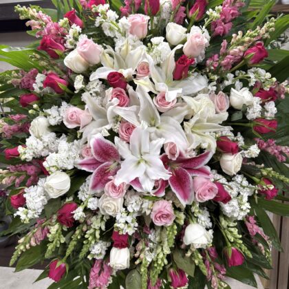 Forever In Our Hearts - Funeral Spray featuring white lilies, pink and red roses, and snapdragons in an elegant arrangement.