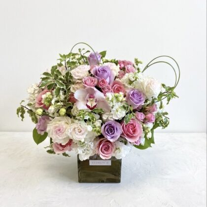 An elegant floral arrangement featuring pink and lavender roses, white peonies, and delicate greenery.