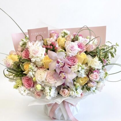 A luxurious bouquet featuring pink and yellow roses, white orchids, and delicate greenery, elegantly arranged.