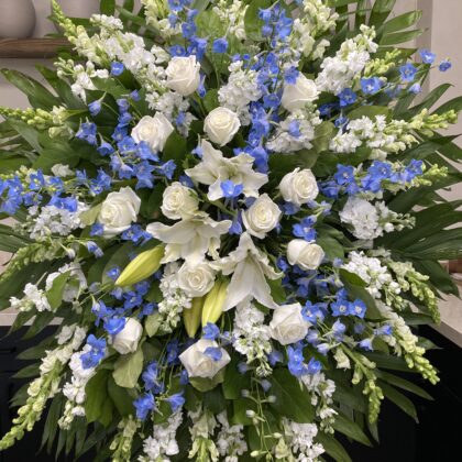 Comforting Cloud Nine Tribute Funeral Spray featuring white roses, lilies, and blue delphinium in an elegant arrangement.