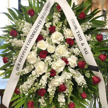 Angel Whispers – Elegant Funeral Spray featuring deep red roses and white stock flowers arranged with lush green foliage.
