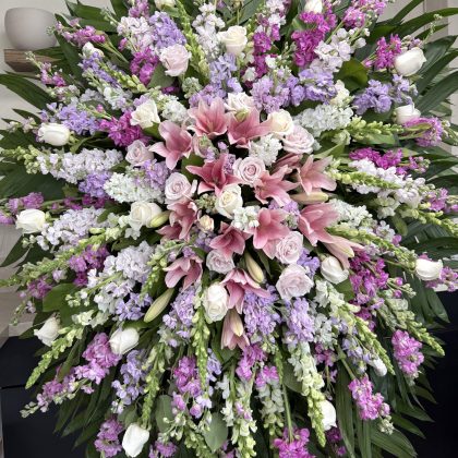 Breathtaking Velvet Petals Funeral Spray featuring pink lilies, white roses, and purple stock flowers in a lush arrangement.
