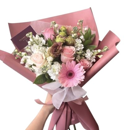 An Elegant Mon Petit Biscuit Wrapped Bouquet featuring pink roses, gerbera daisies, and white stock flowers.