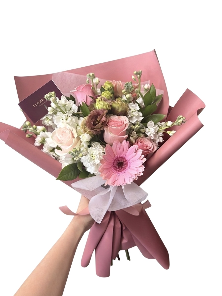 An Elegant Mon Petit Biscuit Wrapped Bouquet featuring pink roses, gerbera daisies, and white stock flowers.