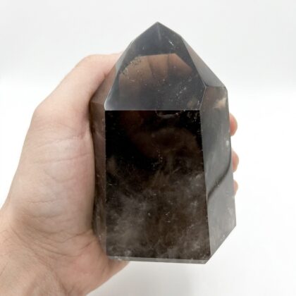A hand holds a polished, translucent Smoky Quartz Point for Spiritual Uplift against a clean white background.