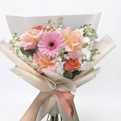 Madame Silhouette – Romantic Wrapped Bouquet featuring peach roses, a pink gerbera daisy, and white filler flowers.