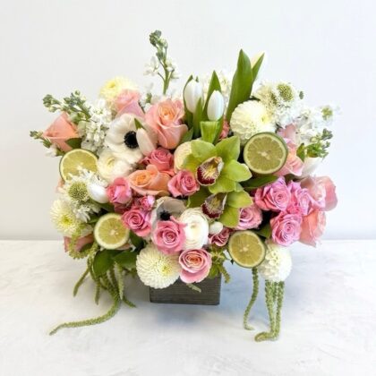 A luxurious floral arrangement of pink roses, white tulips, and green orchids accented with fresh lime slices.