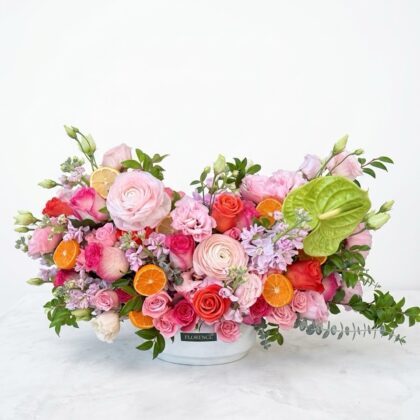 A luxurious floral arrangement of pink roses, ranunculus, and citrus slices in a white Florence-branded ceramic bowl.