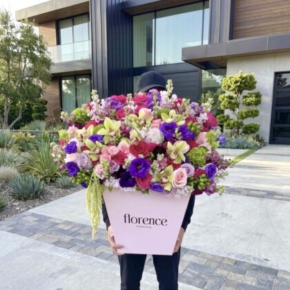 A person holds a Palazzo Dream - Grand Flower Box filled with vibrant pink, purple, and lime green floral blooms.